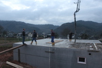 Men stand on the concrete base as concrete is poured from a pipe